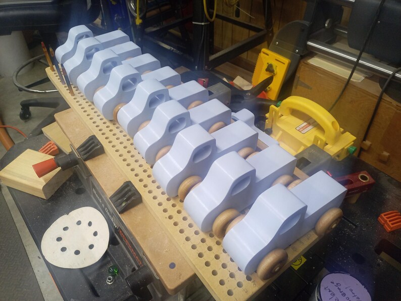 A row of pale blue wooden toy pickup trucks with amber-finished wheels lined up on a perforated board in the workshop.
