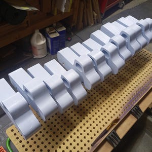 A row of wooden toy pickup bodies coated in pale blue paint rests on a perforated board in the workshop, awaiting wheels and axles.