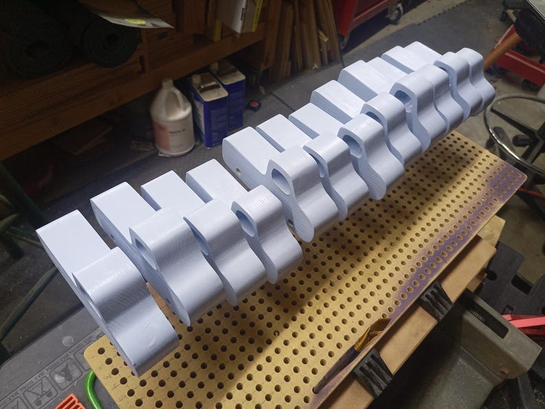 A row of wooden toy pickup bodies coated in pale blue paint rests on a perforated board in the workshop, awaiting wheels and axles.