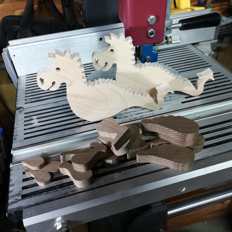 Two freshly cut wooden baby dragon bodies with contrasting hardwood wings, arms, legs, and ears arranged on a Shopsmith bandsaw table.