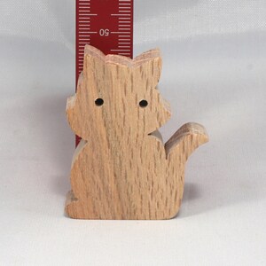 May include: A wooden cat figurine, carved from light brown wood with a natural grain pattern. The cat is sitting with its tail curled around its body.