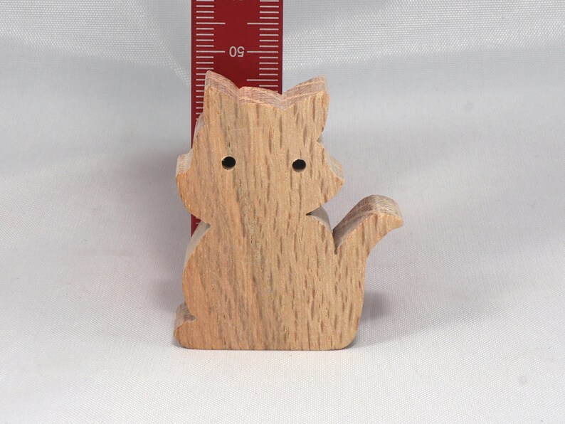 May include: A wooden cat figurine, carved from light brown wood with a natural grain pattern. The cat is sitting with its tail curled around its body.