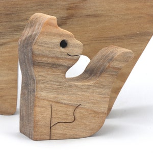 A freestanding wooden puzzle cut in the shape of a large cat standing on four legs. Two smaller kitten figures nest on the large cat’s back and interlock as puzzle pieces. Simple drilled holes form the eyes and nose on each cat, with a shallow cut line for the mouth on the large cat. The completed puzzle stands upright on a plain white surface. Handmade by Odin’s Toy Factory In Tallahassee, Florida, USA.
