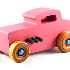 This is a handmade wooden Hot Rod '32 Deuce Coupe toy car. It is hand-painted hot pink with black and metallic sapphire blue trim. The hardwood wheels are finished with nonmarring amber shellac.