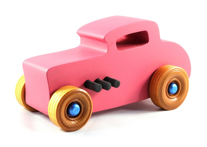This is a handmade wooden Hot Rod '32 Deuce Coupe toy car. It is hand-painted hot pink with black and metallic sapphire blue trim. The hardwood wheels are finished with nonmarring amber shellac.
