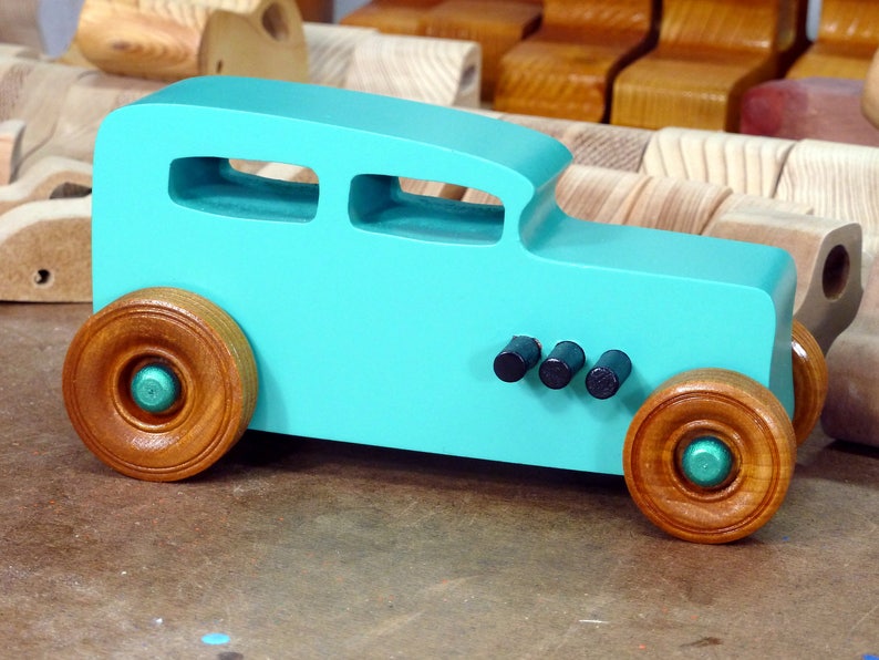 Handmade wooden toy car, 1932 Hot Rod Sedan, painted turquoise with metallic green and black trim. The wheels are finished with nonmarring amber shellac. Handcrafted from natural wood in Tallahassee, Florida, USA. Approximate size: 6 inches long, 3 inches high, 2.5 inches wide. Odin's Toy Factory custom wooden toy.