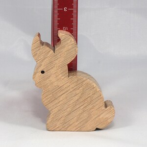 May include: A wooden rabbit figurine, approximately 3 inches tall, with a light brown finish. The rabbit is sitting upright with its ears perked up.