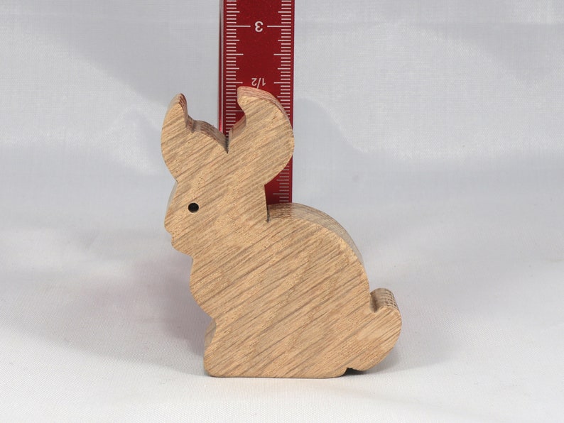 May include: A wooden rabbit figurine, approximately 3 inches tall, with a light brown finish. The rabbit is sitting upright with its ears perked up.