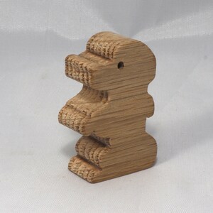 May include: A wooden toy shaped like a standing bear. The bear is made of light brown wood and has a simple, carved design.