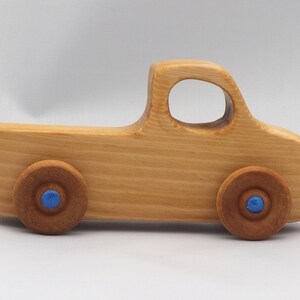 Wooden toy pickup truck from the Play Pal Collection at Odin's Toy Factory. Made from natural wood, finished with amber shellac, and accented with metallic sapphire blue acrylic paint on the wheel hubs. Made In The USA. Approximate dimensions: length 3-1/2 inches, height 1-3/8 inches, width 1-1/2 inches, wheels 3/4 inch diameter. Handmade in Tallahassee, Florida. Natural wood grain and color variations.