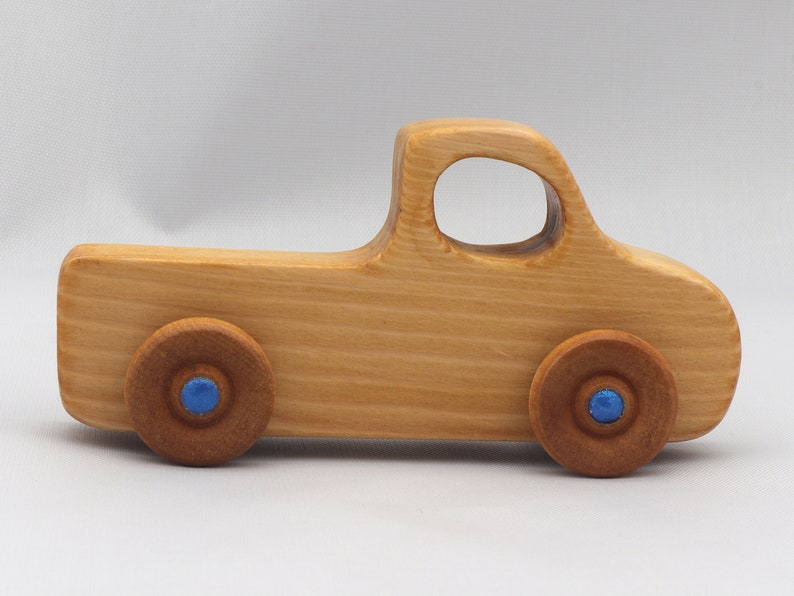 Wooden toy pickup truck from the Play Pal Collection at Odin's Toy Factory. Made from natural wood, finished with amber shellac, and accented with metallic sapphire blue acrylic paint on the wheel hubs. Made In The USA. Approximate dimensions: length 3-1/2 inches, height 1-3/8 inches, width 1-1/2 inches, wheels 3/4 inch diameter. Handmade in Tallahassee, Florida. Natural wood grain and color variations.