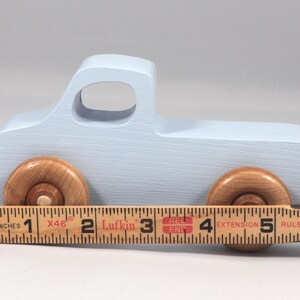 May include: A light blue wooden toy truck with natural wood wheels. The truck measures approximately 5 inches in length. The toy truck has a classic design, perfect for imaginative play.