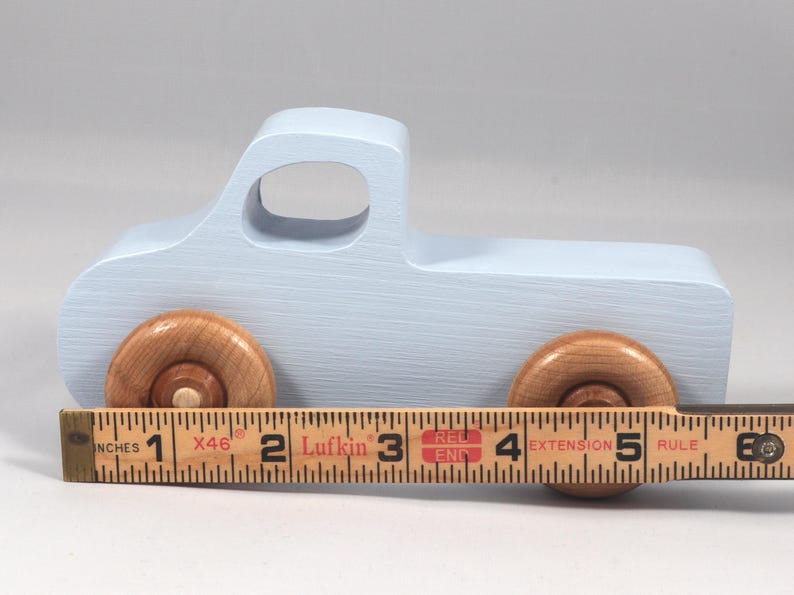 May include: A light blue wooden toy truck with natural wood wheels. The truck measures approximately 5 inches in length. The toy truck has a classic design, perfect for imaginative play.