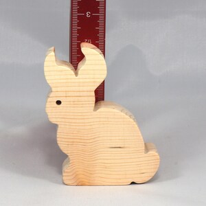 May include: A wooden rabbit figurine, approximately 3 inches tall, with a simple, carved design. The rabbit is light brown and has a smooth, unfinished surface.