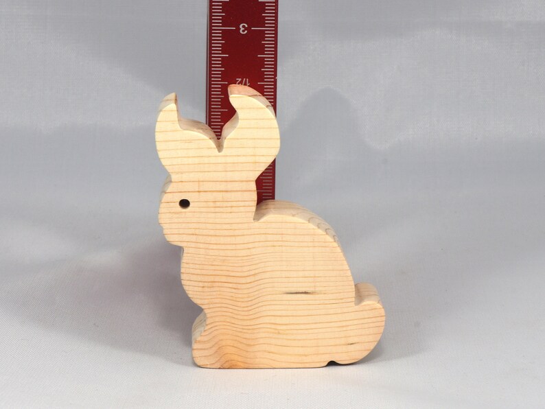 May include: A wooden rabbit figurine, approximately 3 inches tall, with a simple, carved design. The rabbit is light brown and has a smooth, unfinished surface.