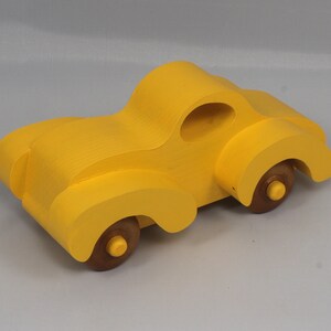 Handmade wooden toy car vintage style of a fat fendered coupe painted bright yellow with nonmarring amber shellac finished wheels. It is an excellent push toy for a younger child.