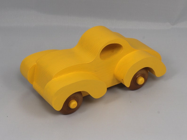 Handmade wooden toy car vintage style of a fat fendered coupe painted bright yellow with nonmarring amber shellac finished wheels. It is an excellent push toy for a younger child.