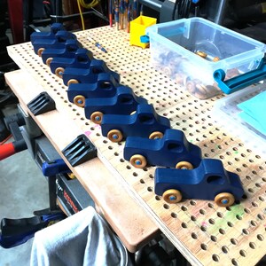 Row of finished navy blue handmade wooden toy pickup trucks with natural wood wheels lined up on my workshop bench.