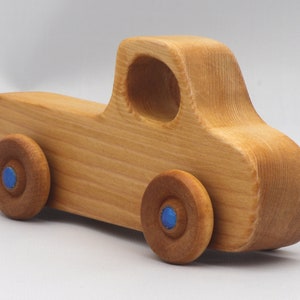 Wooden toy pickup truck from the Play Pal Collection at Odin's Toy Factory. Made from natural wood, finished with amber shellac, and accented with metallic sapphire blue acrylic paint on the wheel hubs. Made In The USA. Approximate dimensions: length 3-1/2 inches, height 1-3/8 inches, width 1-1/2 inches, wheels 3/4 inch diameter. Handmade in Tallahassee, Florida. Natural wood grain and color variations.