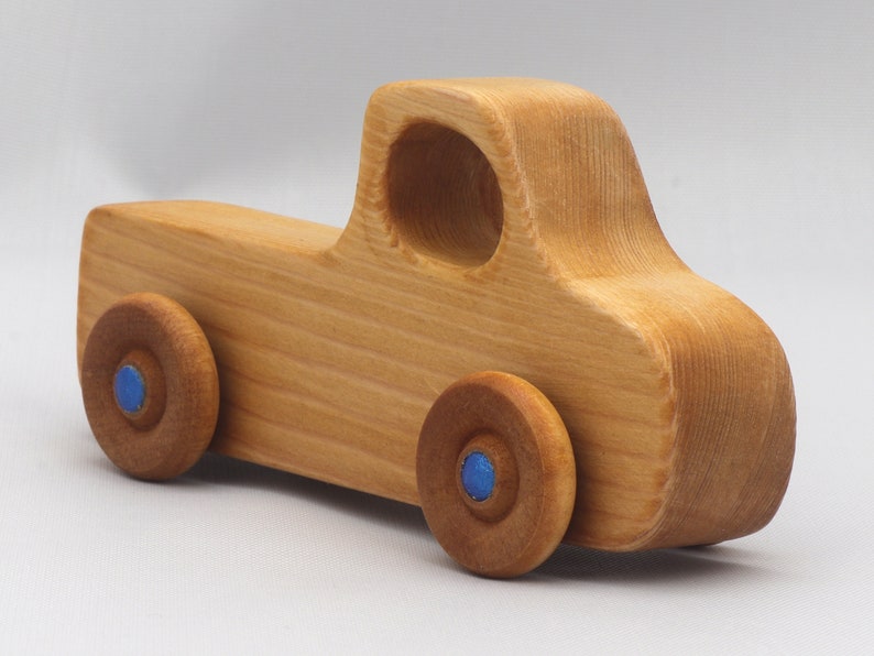 Wooden toy pickup truck from the Play Pal Collection at Odin's Toy Factory. Made from natural wood, finished with amber shellac, and accented with metallic sapphire blue acrylic paint on the wheel hubs. Made In The USA. Approximate dimensions: length 3-1/2 inches, height 1-3/8 inches, width 1-1/2 inches, wheels 3/4 inch diameter. Handmade in Tallahassee, Florida. Natural wood grain and color variations.