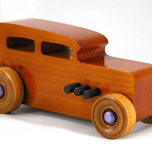 This is a handmade wooden toy car modeled after a Hot Rod 1932 Ford Sedan. It is made from wood, finished with multiple coats of amber shellac, and trimmed with black and metallic purple acrylic paint.