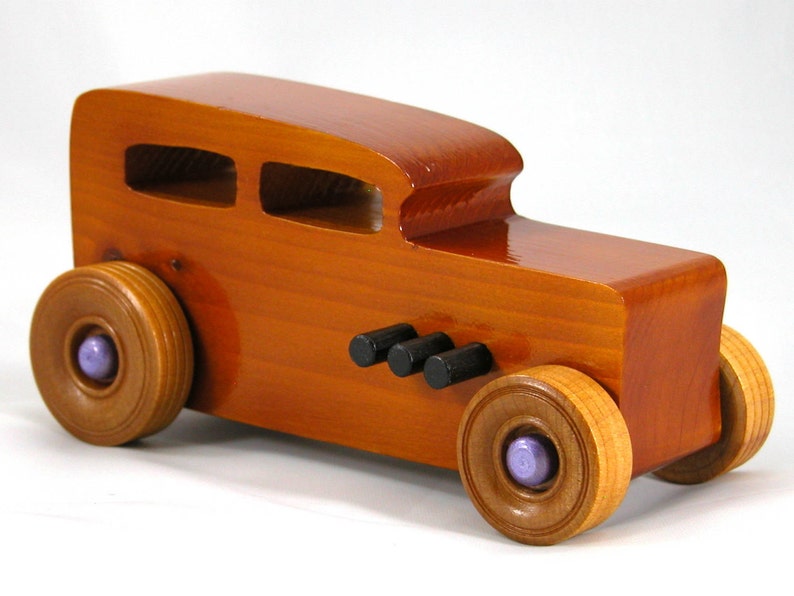 This is a handmade wooden toy car modeled after a Hot Rod 1932 Ford Sedan. It is made from wood, finished with multiple coats of amber shellac, and trimmed with black and metallic purple acrylic paint.