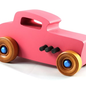 This is a handmade wooden Hot Rod '32 Deuce Coupe toy car. It is hand-painted hot pink with black and metallic sapphire blue trim. The hardwood wheels are finished with nonmarring amber shellac.