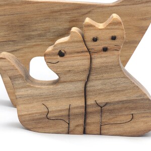A freestanding wooden puzzle cut in the shape of a large cat standing on four legs. Two smaller kitten figures nest on the large cat’s back and interlock as puzzle pieces. Simple drilled holes form the eyes and nose on each cat, with a shallow cut line for the mouth on the large cat. The completed puzzle stands upright on a plain white surface. Handmade by Odin’s Toy Factory In Tallahassee, Florida, USA.
