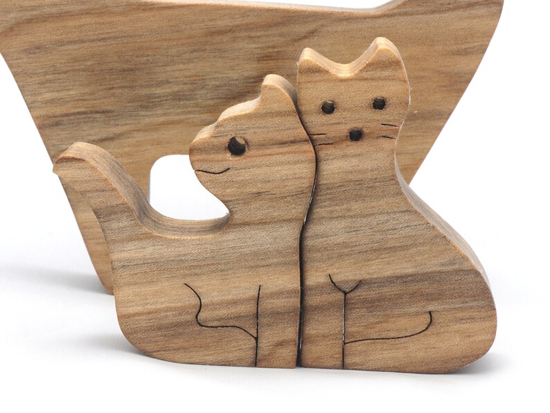 A freestanding wooden puzzle cut in the shape of a large cat standing on four legs. Two smaller kitten figures nest on the large cat’s back and interlock as puzzle pieces. Simple drilled holes form the eyes and nose on each cat, with a shallow cut line for the mouth on the large cat. The completed puzzle stands upright on a plain white surface. Handmade by Odin’s Toy Factory In Tallahassee, Florida, USA.