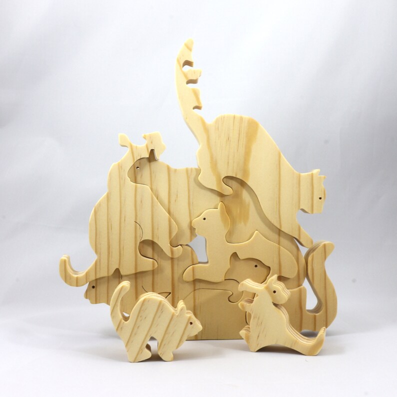 Handmade wooden puzzle featuring several cat-shaped pieces stacked on top of each other in various playful poses, forming a balanced tower. The cats are crafted with smooth edges and natural wood tones, highlighting their unique shapes and expressions.