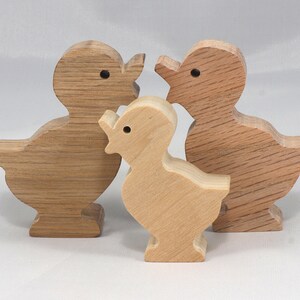 May include: Three wooden duck figurines, one larger than the other two. The larger duck is brown, the smaller ducks are a lighter brown.
