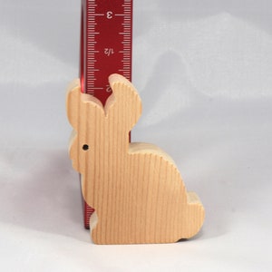 May include: A wooden rabbit figurine, approximately 3 inches tall, with a light brown color and a smooth, natural finish.