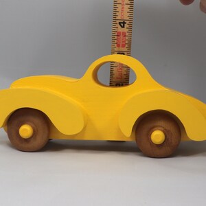 Handmade wooden toy car vintage style of a fat fendered coupe painted bright yellow with nonmarring amber shellac finished wheels. It is an excellent push toy for a younger child.
