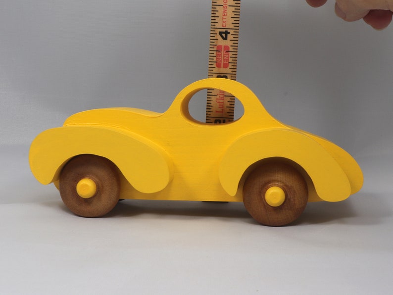 Handmade wooden toy car vintage style of a fat fendered coupe painted bright yellow with nonmarring amber shellac finished wheels. It is an excellent push toy for a younger child.