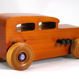This is a handmade wooden toy car modeled after a Hot Rod 1932 Ford Sedan. It is made from wood, finished with multiple coats of amber shellac, and trimmed with black and metallic purple acrylic paint.