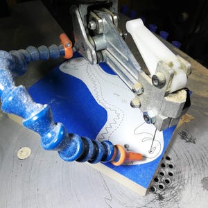Baby dragon body being hand-cut on a scroll saw from a hardwood blank covered with blue painter’s tape and a paper pattern.