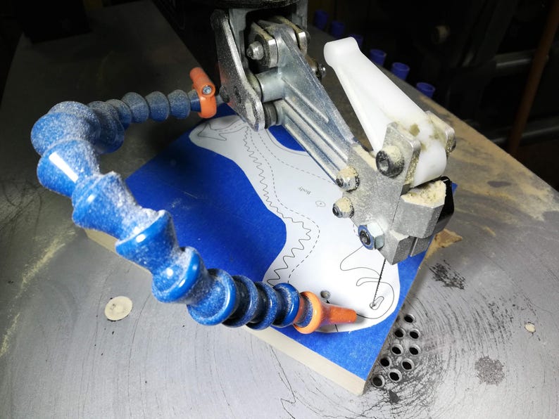 Baby dragon body being hand-cut on a scroll saw from a hardwood blank covered with blue painter’s tape and a paper pattern.
