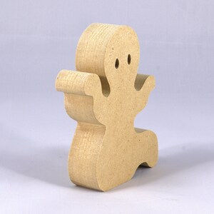 A handmade, unpainted wooden ghost cutout stands upright on a white background. The light-colored solid wood figure has a rounded head with two circular eye cutouts, raised wavy arms, and a curved wavy base, ready for painting or crafting.