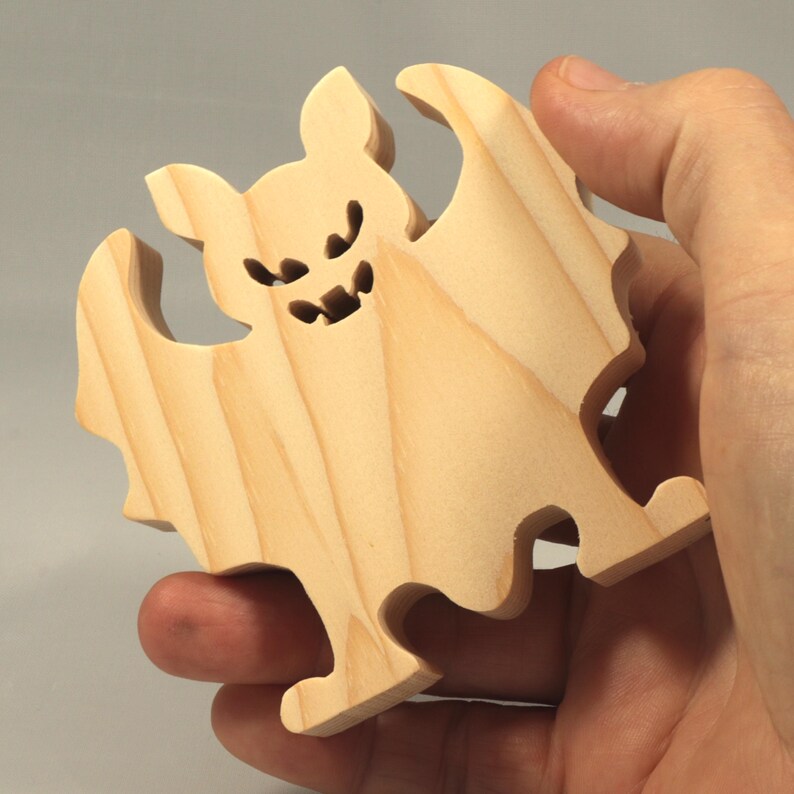 Handmade unpainted wooden Halloween bat cutout, freestanding light-colored solid wood figure with spooky carved face and outstretched wings, ready to paint, from my Snazzy Spooks collection. Held in the makers hand.