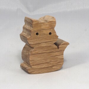 May include: A wooden cat figurine carved from light brown wood. The cat is sitting with its tail curled around its body. The figurine has a simple, minimalist design.