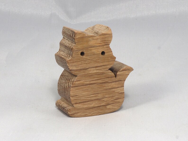 May include: A wooden cat figurine carved from light brown wood. The cat is sitting with its tail curled around its body. The figurine has a simple, minimalist design.