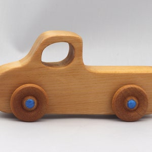 Wooden toy pickup truck from the Play Pal Collection at Odin's Toy Factory. Made from natural wood, finished with amber shellac, and accented with metallic sapphire blue acrylic paint on the wheel hubs. Made In The USA. Approximate dimensions: length 3-1/2 inches, height 1-3/8 inches, width 1-1/2 inches, wheels 3/4 inch diameter. Handmade in Tallahassee, Florida. Natural wood grain and color variations.