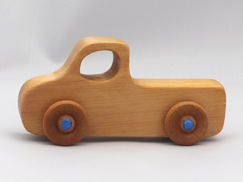 Wooden toy pickup truck from the Play Pal Collection at Odin's Toy Factory. Made from natural wood, finished with amber shellac, and accented with metallic sapphire blue acrylic paint on the wheel hubs. Made In The USA. Approximate dimensions: length 3-1/2 inches, height 1-3/8 inches, width 1-1/2 inches, wheels 3/4 inch diameter. Handmade in Tallahassee, Florida. Natural wood grain and color variations.
