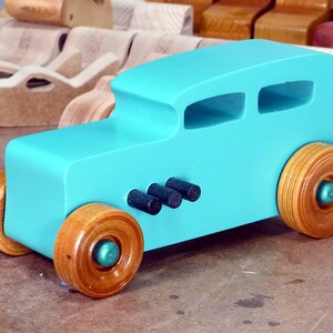 Handmade wooden toy car, 1932 Hot Rod Sedan, painted turquoise with metallic green and black trim. The wheels are finished with nonmarring amber shellac. Handcrafted from natural wood in Tallahassee, Florida, USA. Approximate size: 6 inches long, 3 inches high, 2.5 inches wide. Odin's Toy Factory custom wooden toy.