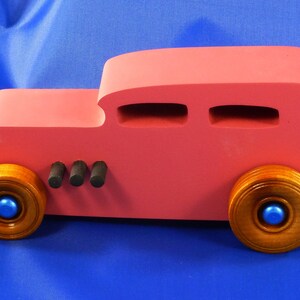 Handcrafted pink wooden hot rod '32 sedan toy car. Features black and metallic sapphire blue accents, and non-marking amber shellac wheels. Made to order for unique play or display.