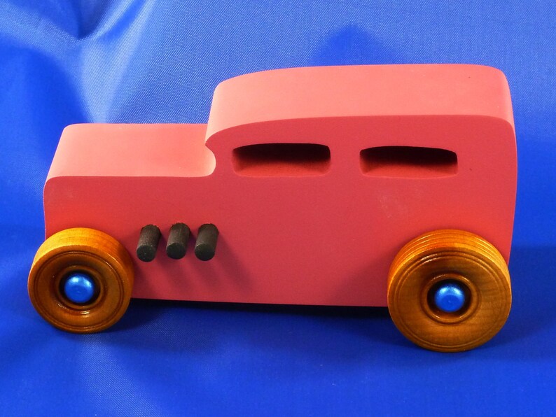 Handcrafted pink wooden hot rod '32 sedan toy car. Features black and metallic sapphire blue accents, and non-marking amber shellac wheels. Made to order for unique play or display.