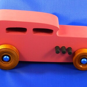 Handcrafted pink wooden hot rod '32 sedan toy car. Features black and metallic sapphire blue accents, and non-marking amber shellac wheels. Made to order for unique play or display.