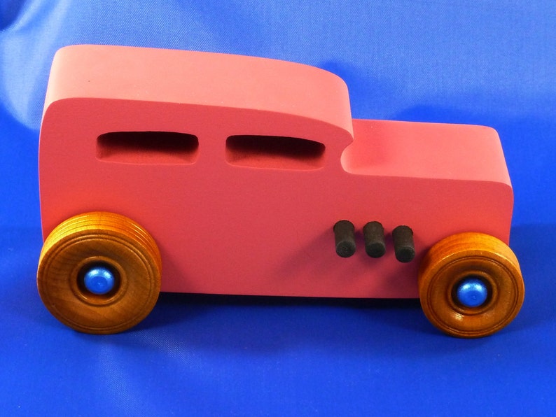 Handcrafted pink wooden hot rod '32 sedan toy car. Features black and metallic sapphire blue accents, and non-marking amber shellac wheels. Made to order for unique play or display.