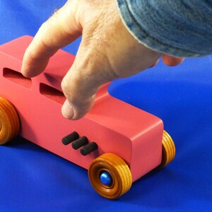 Handcrafted pink wooden hot rod '32 sedan toy car. Features black and metallic sapphire blue accents, and non-marking amber shellac wheels. Made to order for unique play or display.