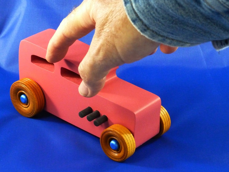 Handcrafted pink wooden hot rod '32 sedan toy car. Features black and metallic sapphire blue accents, and non-marking amber shellac wheels. Made to order for unique play or display.